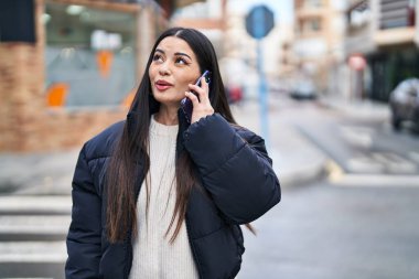 Young beautiful hispanic woman talking on smartphone with relaxed expression at street