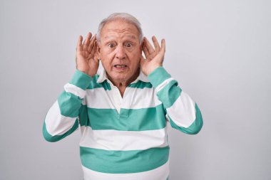 Beyaz arka planda gri saçlı son sınıf öğrencisi iki elini de kulak hareketi yaparken duymaya çalışıyor. Dedikoduya meraklı. İşitme sorunu, sağır 