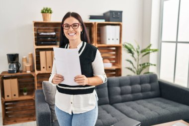 Young beautiful hispanic woman business worker reading document at office