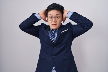 Genç Asyalı takım elbiseli, kravatlı çılgın ve elleri başında korkmuş, ağzı açık şoktan korkan ve şaşıran bir adam. 