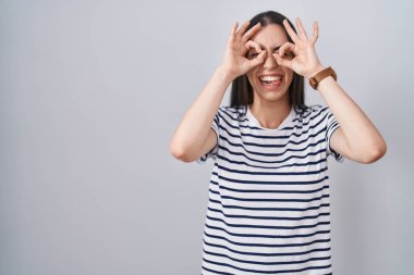 Genç esmer kadın çizgili tişört giyiyor dürbün gibi jest yapıyor, gözleri parmaklarından bakıyor. çılgın ifade. 