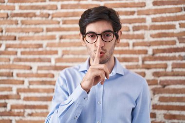 Tuğla duvar arkasında dikilen genç İspanyol adam parmakları dudaklarında sessiz olmak istiyor. sessizlik ve gizli konsept. 