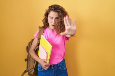 Öğrenci çantası takan ve elinde kitap tutan beyaz bir kadın avuç içi hareketlerini durduruyor, kızgın ve hayal kırıklığına uğramış bir ifade takınıyor. 