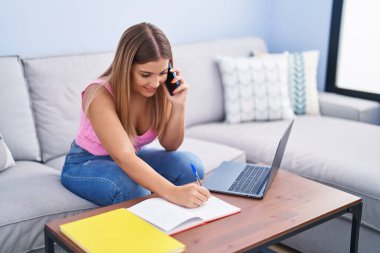 Genç, güzel İspanyol kız öğrenci akıllı telefondan konuşuyor. Evdeki defterde yazıyor.