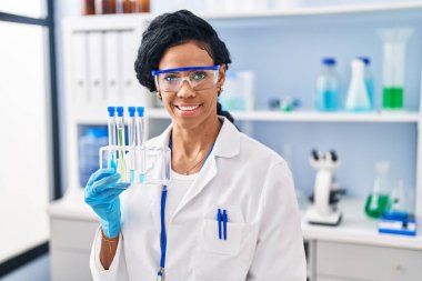 Orta yaşlı İspanyol kadın, laboratuarda çalışıyor. Pozitif ve mutlu görünüyor. Gülümsüyor ve kendine güvenen bir gülümsemeyle dişlerini gösteriyor. 