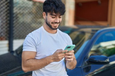 Young hispanic man using smartphone leaning on car at street