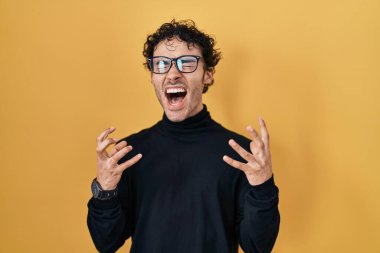 İspanyol adam sarı arka planda duruyor deli deli deli bağırıyor ve bağırıyor agresif bir ifade ve kollar havada. hüsran kavramı. 