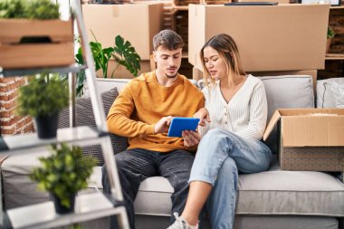 Young man and woman couple using touchpad sitting on sofa at new home