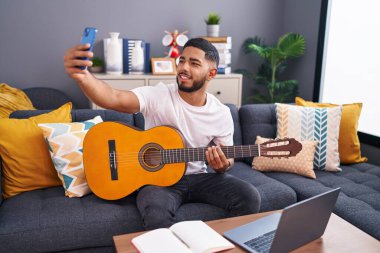 İnternet 'te klasik gitar dersi alan genç latin adam evde akıllı telefondan selfie çekiyor.