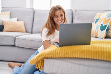 Young blonde girl using laptop sitting on floor at home