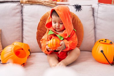 Evdeki kanepede oturan balkabağı kostümü giyen sevimli İspanyol çocuk.