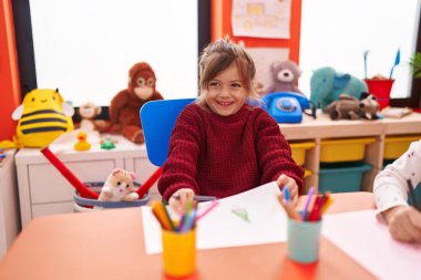 Anaokulunda masaya oturmuş kağıda resim çizen sevimli İspanyol kız öğrenci.