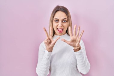 Pembe arka planda beyaz süveter giyen genç sarışın kadın sekiz numaralı parmaklarını gösterip işaret ederken kendinden emin ve mutlu gülümsüyor.. 