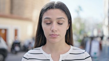 Young beautiful hispanic woman breathing with closed eyes at street
