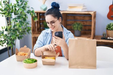 Kafkasyalı genç bir kadın evde akıllı telefon kullanarak yemek yiyor.