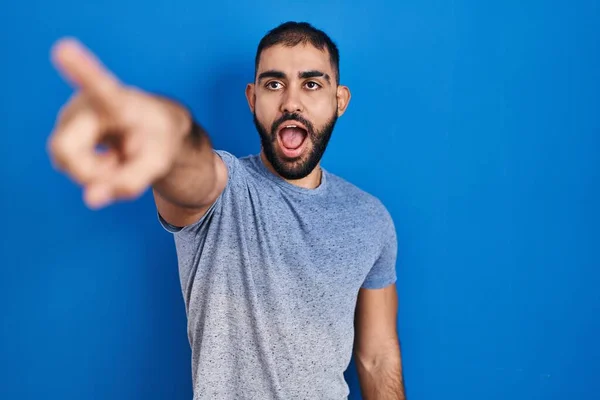 中東の男のひげの青の背景の上に指を前に 口を開けて驚いて表現を指して立って 何かの前に — ストック写真