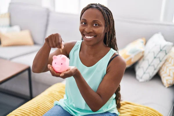 African American Woman Inserting Coin Piggy Bank Sitting Sofa Home — Stock Photo, Image