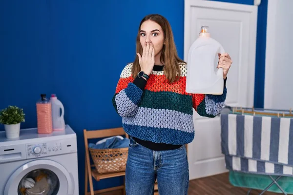Young Hispanic Girl Holding Detergent Bottle Covering Mouth Hand Shocked — Stock Photo, Image
