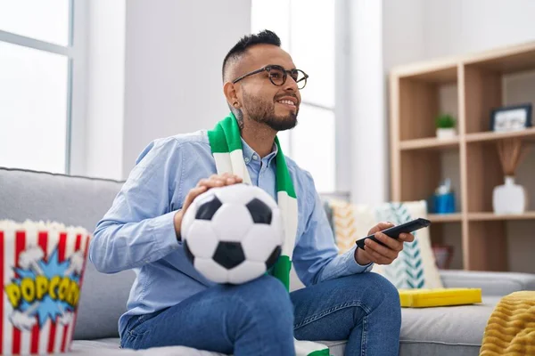 stock image Young hispanic man football hooligan holding ball supporting team smiling with a happy and cool smile on face. showing teeth. 