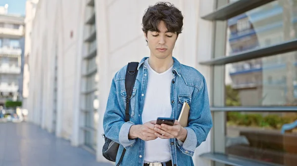 Young hispanic man student using smartphone with relaxed expression at university