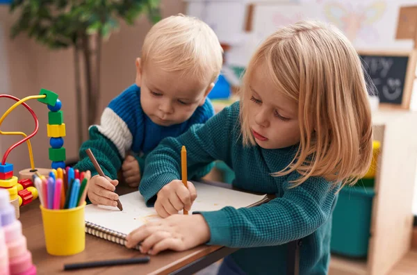 幼稚園の机に座って紙絵を描く大人の男の子と女の子 — ストック写真