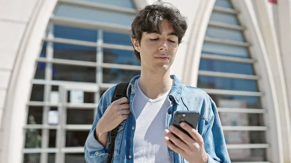 大学でリラックスした表情のスマートフォンを使用して若いヒスパニック系の男学生 — ストック写真