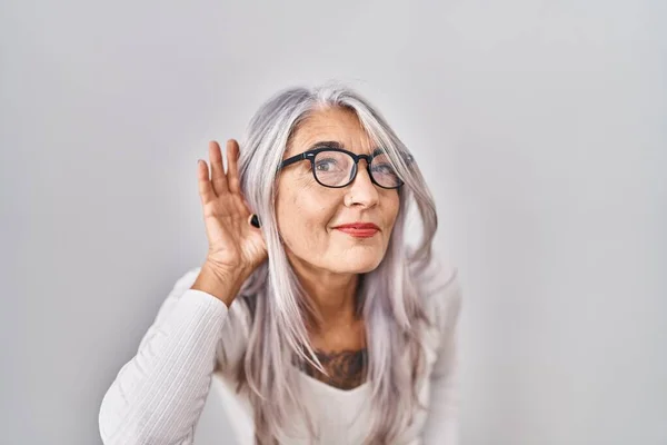 白髪の中年女性が白地の上に立ち 噂やゴシップに耳を傾ける耳の上に手で笑っています 聴覚障害の概念 — ストック写真