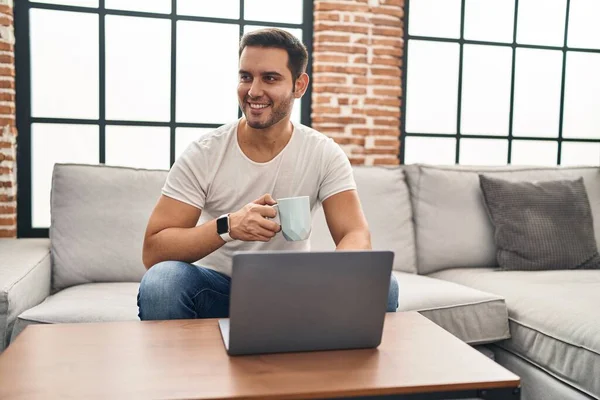 Young Hispanic Man Using Laptop Drinking Coffee Sitting Sofa Home — Stockfoto