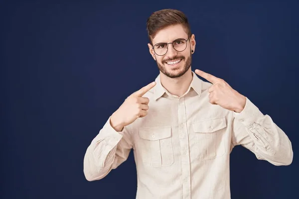 stock image Hispanic man with beard standing over blue background smiling cheerful showing and pointing with fingers teeth and mouth. dental health concept. 