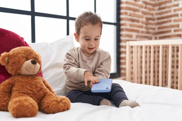 可爱的他的惊慌失措的男孩拿着智能手机坐在卧室的床上 — 图库照片