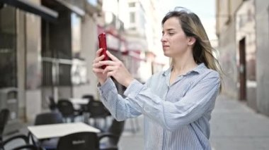 Kendine güvenen genç sarışın kadın kahve dükkanının terasında akıllı telefondan fotoğraf çekiyor.