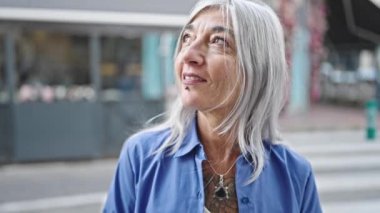 Orta yaşlı, gri saçlı, gülümseyen bir kadın kahve dükkanının terasında kendine güveniyor.