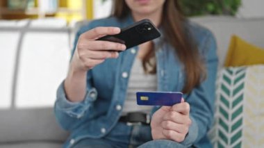 Genç ve güzel İspanyol kadın evde akıllı telefonuyla kredi kartına fotoğraf çekiyor.
