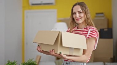 Genç sarışın kadın yeni evinde kendine güvenen bir paket tutuyor.