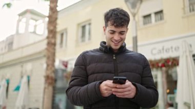 Kafe terasında gülümseyen akıllı telefon kullanan genç bir İspanyol.