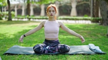 Genç kızıl saçlı kadın yoga egzersizi yapıyor parkta otun üzerinde oturuyor.