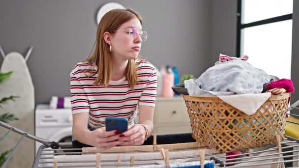 Mujer Rubia Joven Usando Teléfono Inteligente Apoyado Tendedero Sala Lavandería — Vídeos de Stock