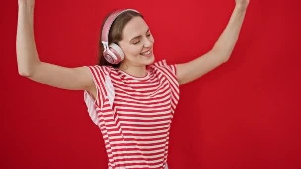 若い金髪の女性は音楽を聴き 孤立した赤い背景の上に踊ります — ストック動画