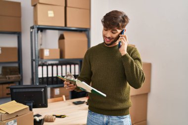 Young arab man ecommerce business worker talking on smartphone reading document at office