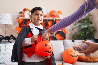Kostümlü sevimli İspanyol çocuk evde balkabağı sepetinde şeker alıyor.