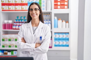 Young beautiful hispanic woman pharmacist smiling confident standing with arms crossed gesture at pharmacy