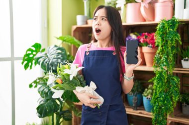 Çiçekçide çalışan genç Çinli kadın akıllı telefon ekranında kızgın ve kızgın çığlıklar atıyor öfkeyle bağırıyor, öfkeyle yukarı bakıyor.. 