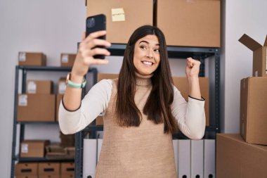 Genç esmer kadın küçük işletmelerde çalışıyor. Selfie çekiyor. Gururla bağırıyor, zaferi ve başarıyı kutluyor. 