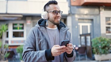 Hispanik adam güler kendine güvenen sokak telefonuyla müzik dinleyen