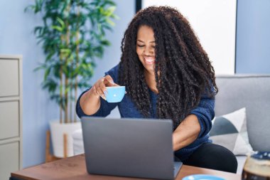 African american woman using laptop drinking coffee at home