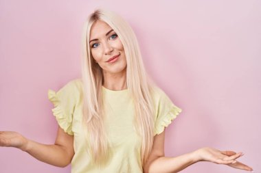 Pembe arka planda duran beyaz bir kadın. Hiçbir fikri olmayan, kolları açık, kafası karışık bir kadın.. 