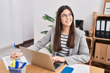 Genç, güzel İspanyol iş kadını. Ofisteki evraklarda dizüstü bilgisayar kullanıyor.