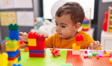 Anaokulundaki masada oturan, inşaat bloklarıyla oynayan sevimli İspanyol çocuk.