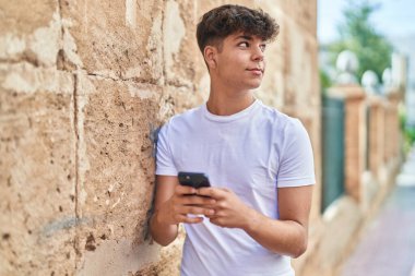 Young hispanic teenager smiling confident using smartphone at street