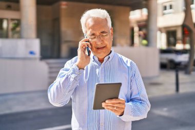 Senior man talking on the smartphone using touchpad at street